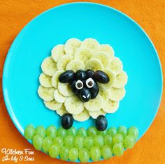 a blue plate topped with grapes and a sheep made out of bananas