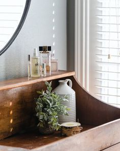 a white vase sitting on top of a wooden shelf next to a mirror and potted plant