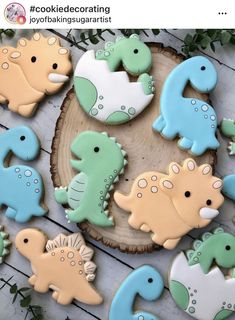 cookies decorated like dinosaurs are on a wooden board next to greenery and leaves in the background