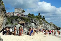 many people are walking on the beach near some cliffs