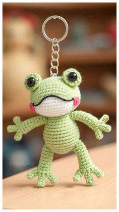 a crocheted frog keychain with a pink flower in its mouth and eyes