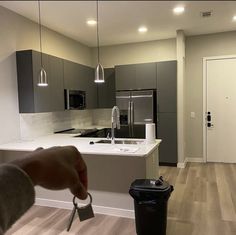 a person is holding a key in front of a kitchen with grey cabinets and white countertops