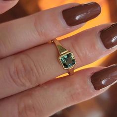 a woman's hand holding a ring with a green gemstone on the middle