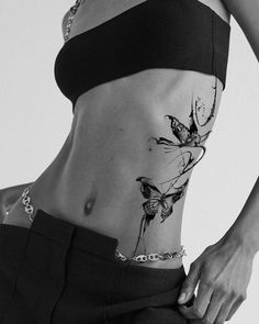 a woman with a butterfly tattoo on her stomach is wearing black pants and a crop top