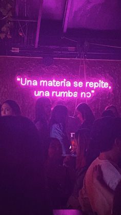 people standing in front of a neon sign that reads una materiale se repito, una rumba no