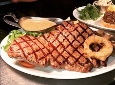 steak, onion rings and salad on a white plate with sauce in the middle is sitting on a table