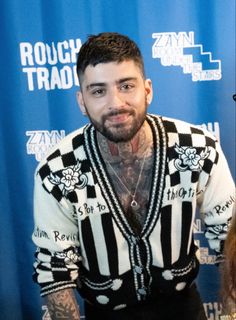 a man with tattoos standing in front of a blue backdrop wearing a black and white sweater