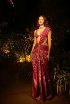 a woman in a red sari posing for the camera at night with lights behind her