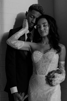 a man and woman standing next to each other in front of a white brick wall