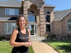 a woman standing in front of a large brick house with grass on the side walk