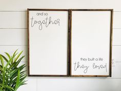 two wooden frames with writing on them next to a potted plant and wall hanging