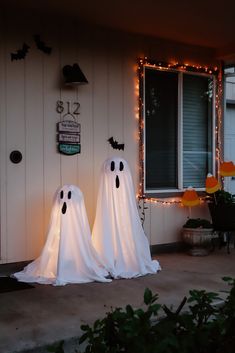 two ghost statues in front of a house decorated for halloween with lights on the windows