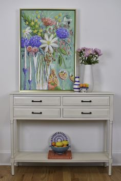 a white table with flowers and fruit on it in front of a framed art piece