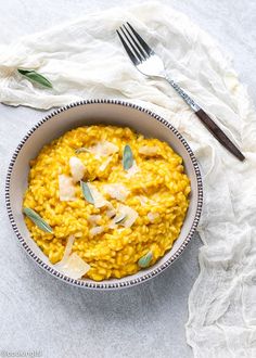 a bowl filled with yellow riso and garnished with sage leaves on top