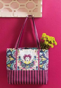 a purse hanging on the wall with flowers in front of it and a pink background