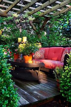 a red couch sitting on top of a wooden deck surrounded by trees and plants in front of a pergolated roof