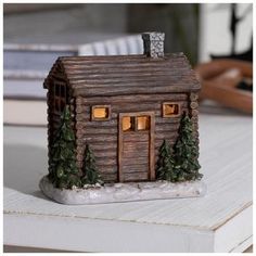 a small wooden house with lights on and trees around the front door is sitting on a table