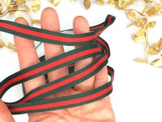 a hand holding a red and black ribbon with gold leaves around it on a white background