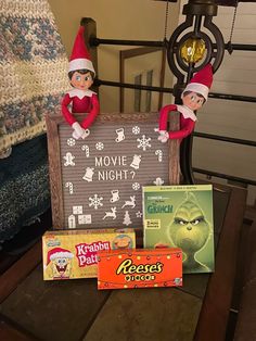 two elfs are sitting on a chair next to some movies and candy bar boxes