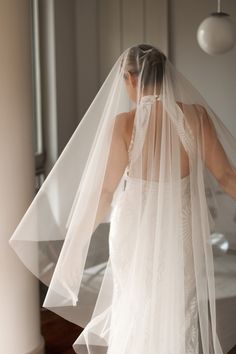 a woman in a wedding dress and veil is looking at the bed with her back turned to the camera