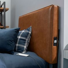 a brown headboard on a bed with blue pillows and a phone plugged in