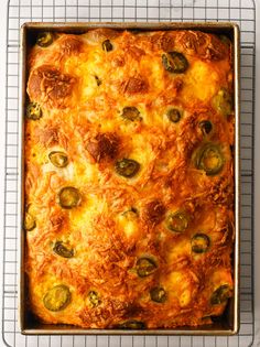 a casserole with cheese and green peppers in a pan on a cooling rack