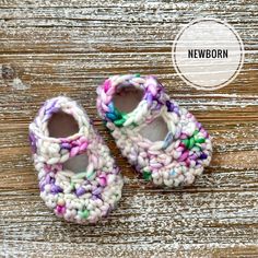 two crocheted baby shoes sitting on top of a wooden floor with the words newborn written