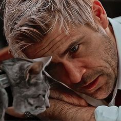 a man holding a cat in his right hand and looking at it's face