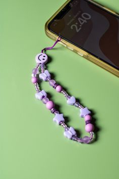 a cell phone is next to a purple and white beaded necklace on a green surface