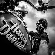 black and white photograph of a man wearing a motorcycle helmet standing next to his bike