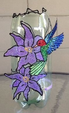 a glass vase with a hummingbird and purple flowers on the front, sitting on a table