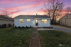 a small blue house sitting on top of a lush green grass covered yard next to a sidewalk