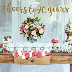 a table topped with lots of vases filled with pink and blue flowers next to a window