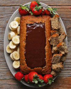 a cake with chocolate frosting surrounded by sliced bananas and strawberries on a plate