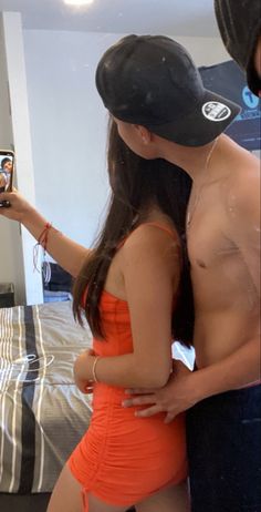 a woman in an orange dress is taking a selfie with her cell phone while standing next to a man