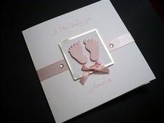 a white card with pink baby feet and ribbon on the front, sitting on top of a black table