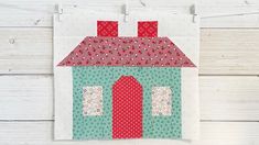 a quilted house with red and green trimmings on a white wooden wall