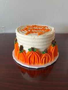 a white cake with orange frosting and pumpkins on it sitting on a wooden table