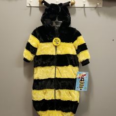 a yellow and black striped onesuit hanging from a hook on a gray wall next to a white coat hanger