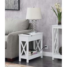 a white end table with a lamp on it next to a gray couch and rug