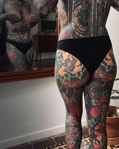 a woman with tattoos on her back and legs standing in front of a bathroom mirror