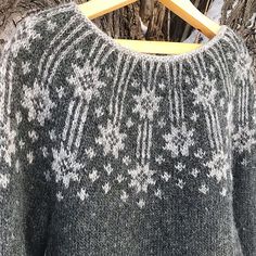 a sweater hanging on a wooden hanger in front of a tree with snowflakes