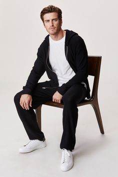 a man sitting on top of a wooden chair wearing white shoes and a black jacket