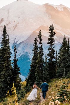 a bride and groom walking down a trail in front of a snow - capped mountain