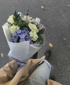 a bouquet of flowers sitting on the back of a person's leg in front of an asphalt road