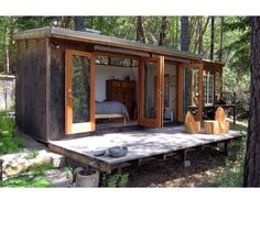 a small cabin in the woods with its doors open and furniture on the ground next to it