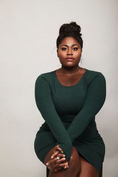 a woman in a green dress sitting on a chair with her legs crossed and looking at the camera