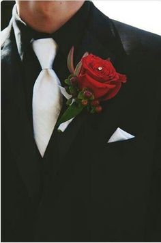 a man wearing a black suit and white tie with a red rose in his lapel