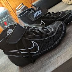 a pair of black and white shoes sitting on top of a wooden table next to a bottle