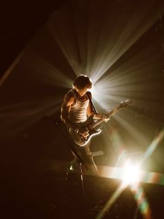 a man with a guitar on stage in the light from his headlamp behind him